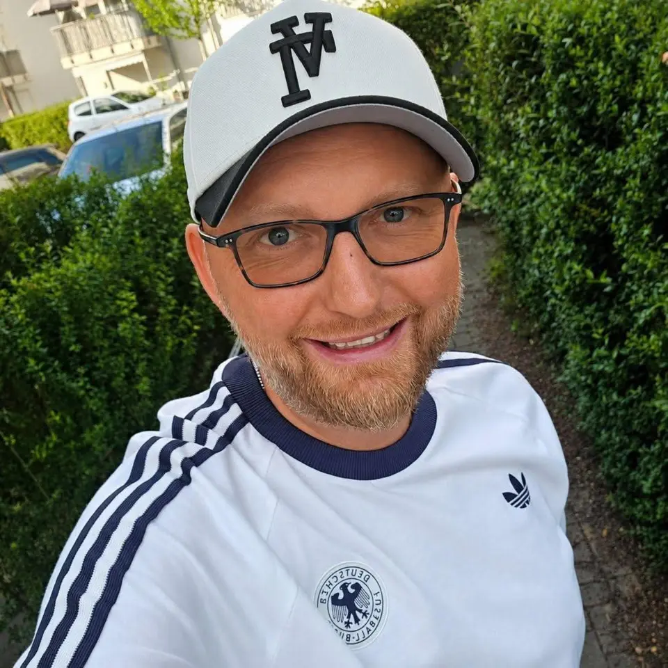 Sascha Frenz lächelt draußen in Cap und Fußballtrikot.